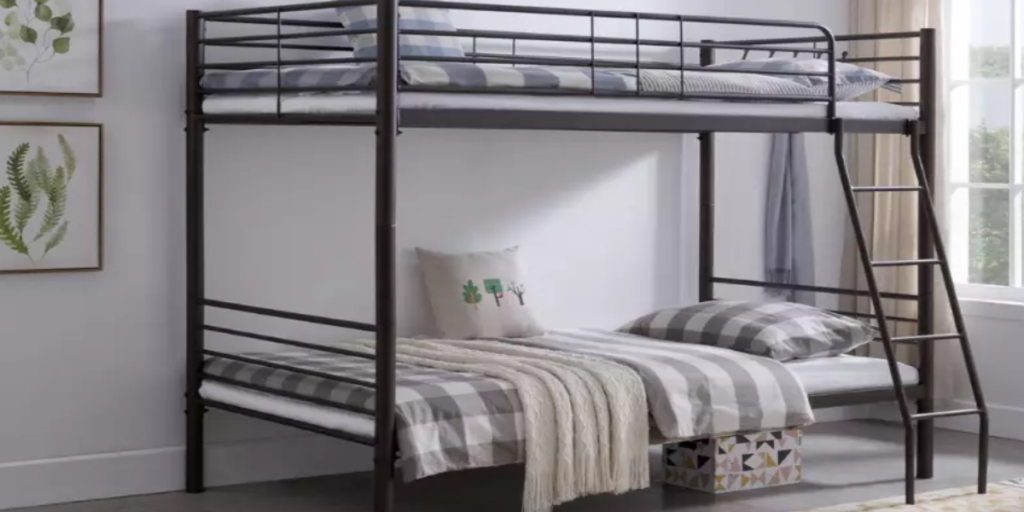 A metal bunk bed with ladder, top bed unmade, bottom bed neatly made, colorful pillows and blankets.