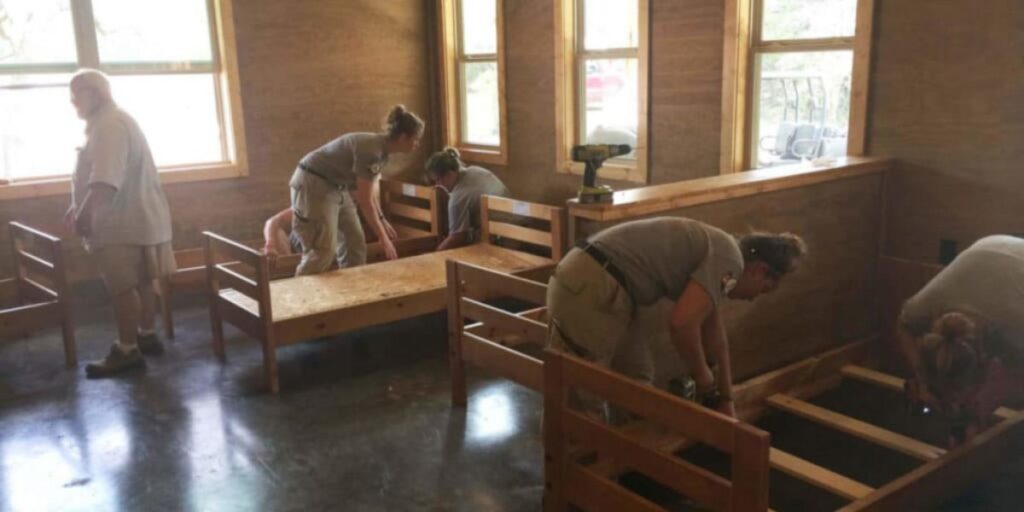 People assembling quick ship furniture on beds in a room with windows. Proper installation is crucial for safety and functionality. Hire professional installers if needed.