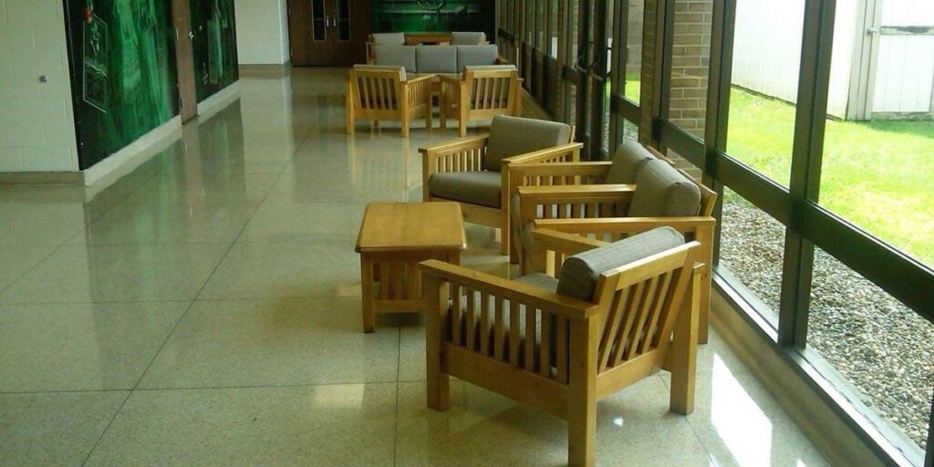 A long hallway featuring wooden chairs and tables, designed for durability and comfort in healthcare settings.