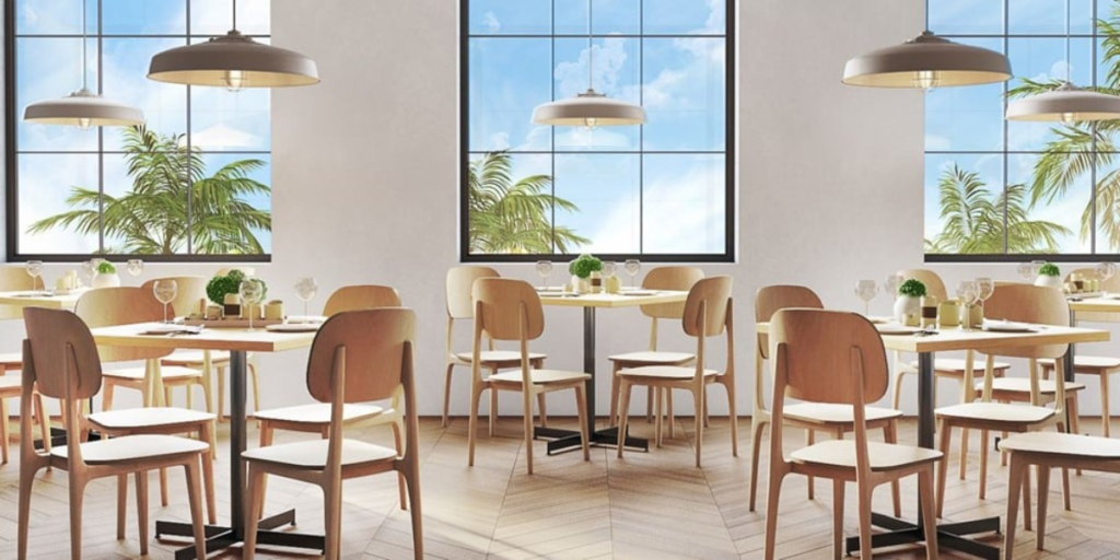 A restaurant featuring tables and chairs arranged near large windows, creating a bright and inviting dining atmosphere.