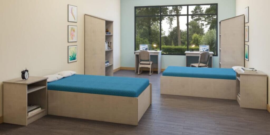 A room featuring two bariatric beds and a sturdy desk, designed for comfort and safety in medical settings.