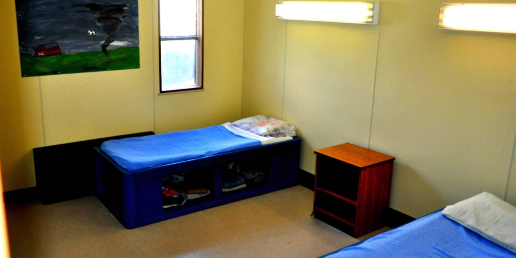 A room featuring two sturdy plastic beds and a painting on the wall, designed for enhanced weight support and stability.