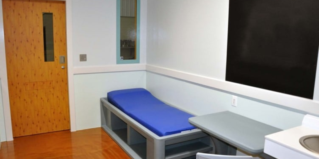 A small room featuring a bed and a sink, emphasizing durability and hygiene in healthcare environments.