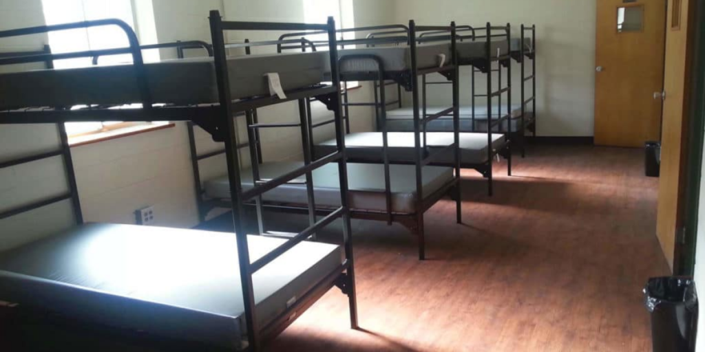 A row of sturdy bunk beds in a room with a door, designed for cost-effective sleep quarters in communal settings.