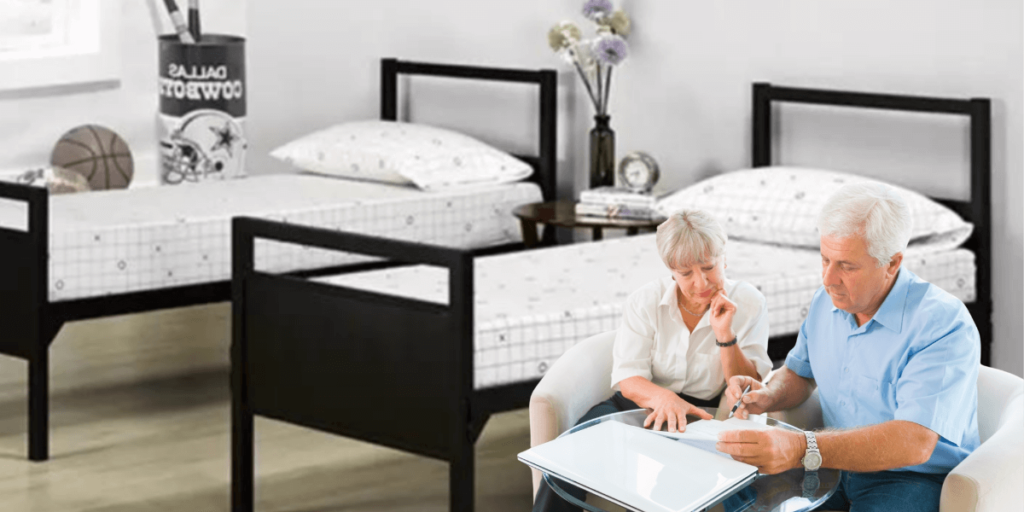 An older couple sits on a bed, using a laptop, engaged in a discussion or activity together.