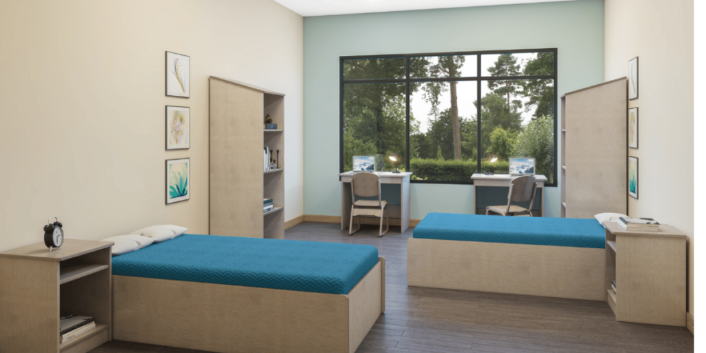 A room featuring two beds and a desk, emphasizing cleanliness and safety for a positive shelter environment.