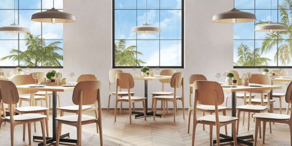 A restaurant featuring tables and chairs arranged in front of large windows, creating a bright and inviting atmosphere.