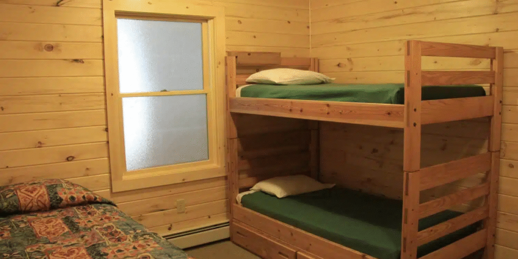 A wooden bunk bed in a cozy cabin, positioned near a window that lets in natural light.